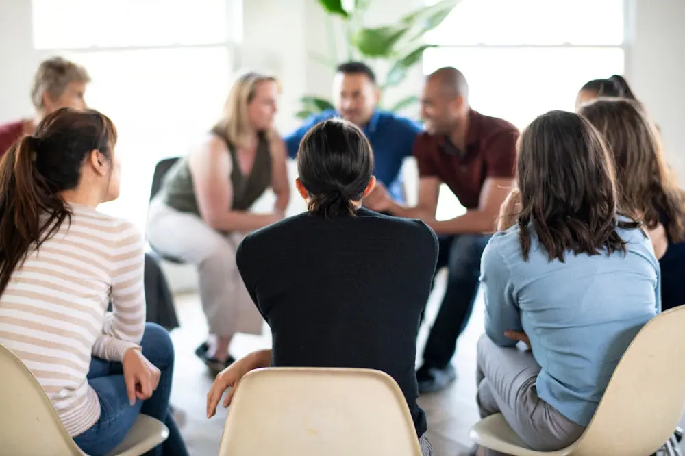 Rear view of circle of group therapy session in brightly lit room.
