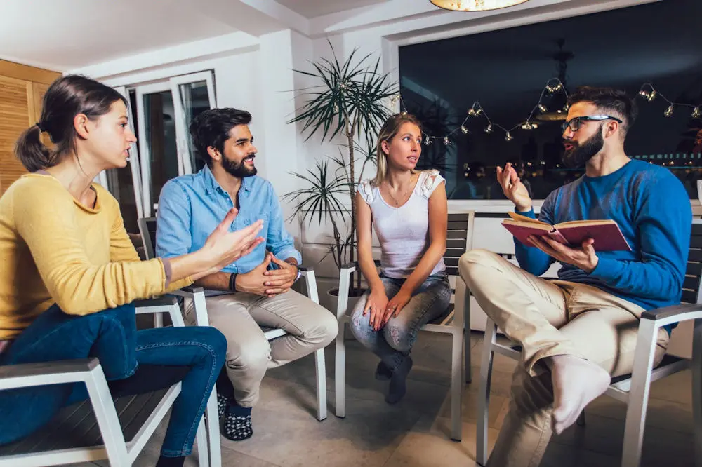 Rear view of circle of group therapy session in brightly lit room.