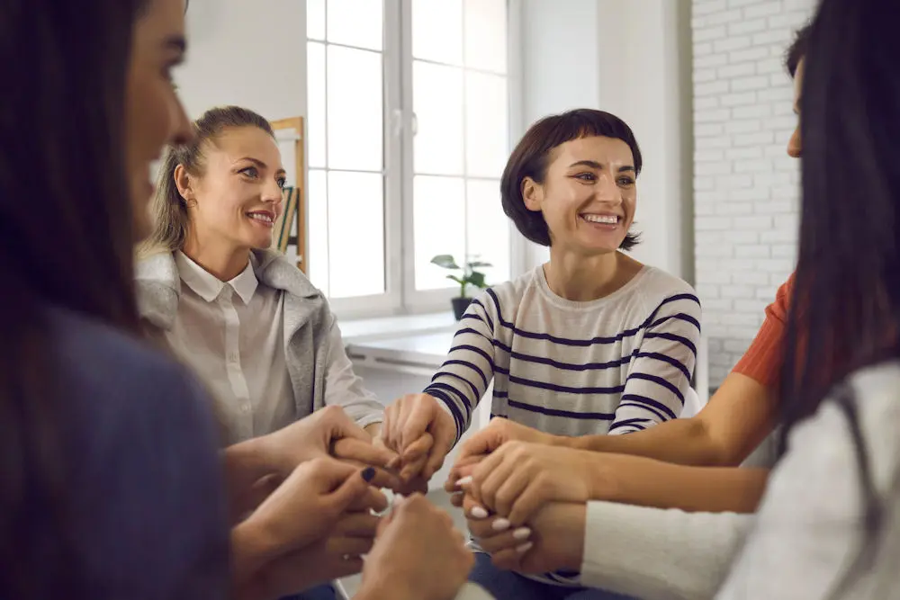 Group of women putting hands in the middle to celebrate finishing CBT treatment.