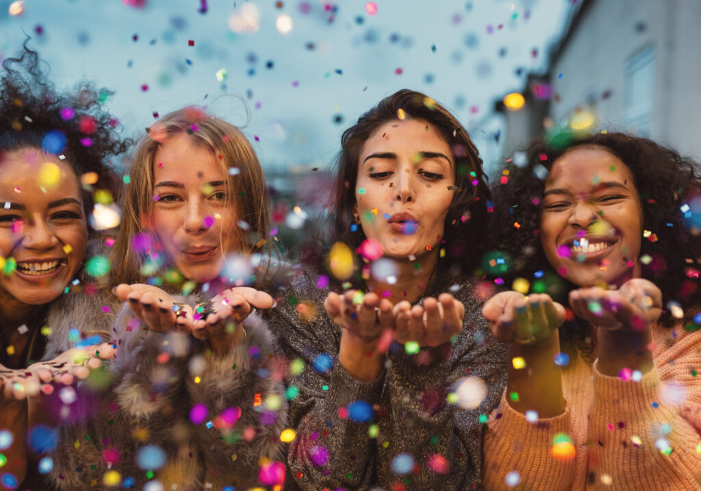 Four women blowing cofetti out for New Year's Eve