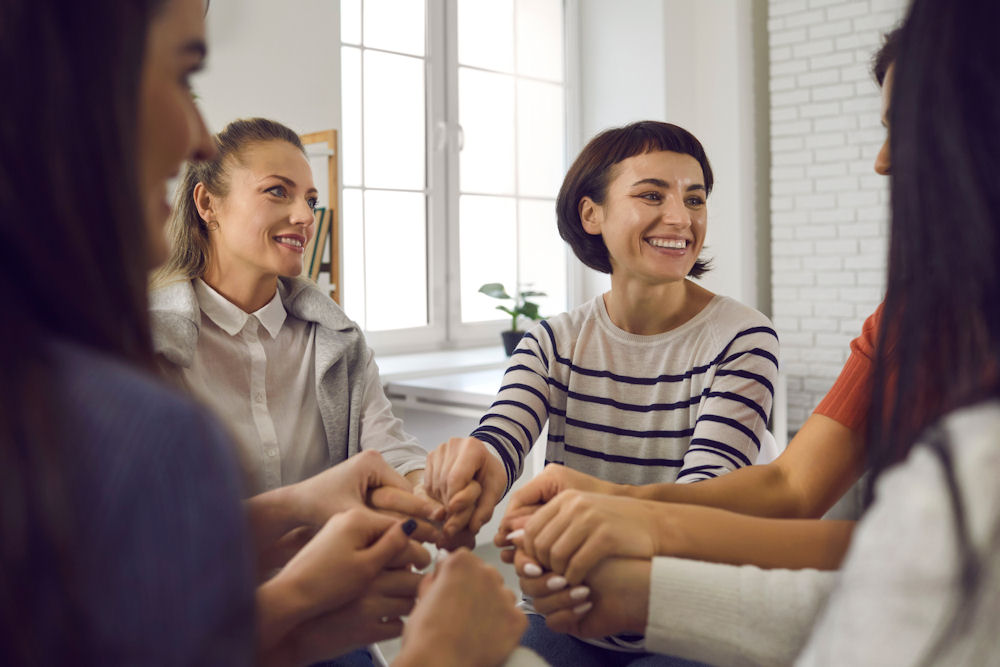 Group of women putting hands in the middle to celebrate finishing CBT treatment.
